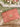 Pink handbag with scalloped edge and gold chain on a wooden surface with white flowers in the background