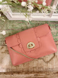 Pink handbag with scalloped edge and gold chain on a wooden surface with white flowers in the background