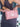 Pink handbag with scalloped edges held by a person wearing a dark dress.