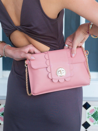 Pink handbag with scalloped edges held by a person wearing a dark dress.