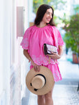 Woman in a pink dress with white embroidery holding a straw hat and mulberry metallic handbag from brand Elyse &i.