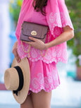 Person wearing a pink dress with white patterns, holding an Elyse & i Mulberry metallic Otis handbag and a straw hat.