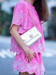 Person wearing a pink dress with white embroidery, holding a silver leather bag by Elyse & i called Otis shell.