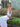 Woman in a white dress sitting on a decorative bench with a green background with a shoulder bag called Otis from brand Elyse & i.