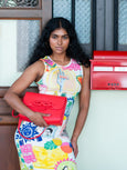 Woman holding an Elyse & i red clutch in front of a building with a red mailbox.