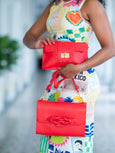 Person holding two red Elyse & i handbags with a colorful dress in the background