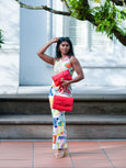 Woman holding Elyse & i red Theo Knot & Finn Scallop handbags in a colorful outfit outdoors