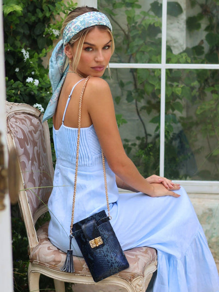 Woman in a light blue dress sitting outdoors with a navy Elyse & i Luna Lock handbag.