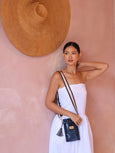 Woman in a white dress holding a navy python print Luna Lock phone bag by Elyse & i against a pink wall with a straw hat.