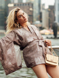 Woman in a patterned outfit holding a gold handbag - the Otis by Elyse & i - in an urban setting