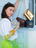 Woman holding a gold Otis handbag with other Elyse & i Otis bags displayed on a light blue door.