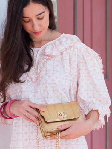 Woman holding a gold Otis handbag by Elyse & i against a pink background