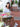 Woman sitting at a table with flowers and an Elyse & i gold Otis handbag, smiling outdoors.