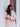 Woman in a white dress holding a gold Elyse & i Otis handbag against a white wall with a red door.