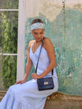 Woman in a light blue dress with an Elyse & i navy snakeprint leather handbag sitting against a textured wall.
