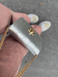Silver handbag by Elyse & i called Otis with gold chain held by a person wearing pink pants on a blurred background