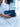 Person holding a blue Elyse & i Nell Knot clutch against a blurred white background