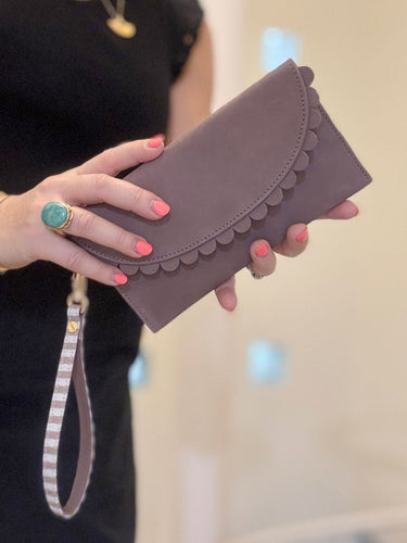 Mauve purse with scallop details being held by a lady with green ring on.