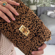cheetah print Finn Scallop clutch by Elyse & i clutch bag with gold buckle held by a hand in a blurred indoor setting