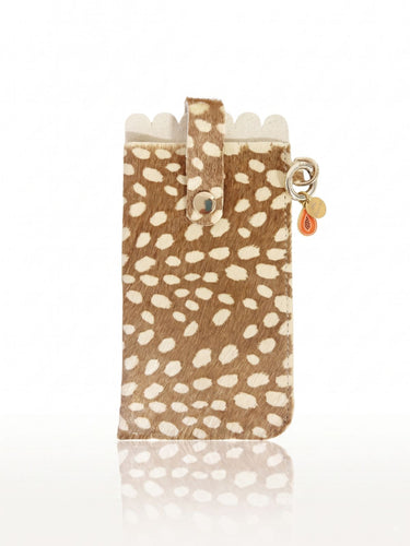 A phone case made of brown and cream spotted hair-on-hide, featuring a scalloped edge, a strap closure with a snap button, and a small gold-tone keychain charm with a teardrop tag, shown on a white background with a reflection.