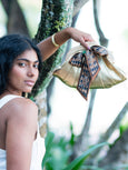 Woman holding a gold Elyse & i Dawn Scallop clutch with a decorative ribbon in a natural setting