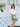 Woman in white blouse and green skirt holding a gold Elyse & i Dawn Scallop purse in front of a white door with blue decorations.
