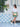Woman in a white top and green skirt standing in front of a white door with blue accents carrying crossbody the gold Elyse & i Dawn Scallop clutch