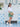 Woman in a white blouse and green skirt standing in front of a white door with decorative blue tiles carrying a gold Elyse & i Dawn Scallop clutch crossbody