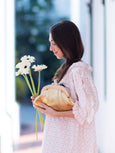 Woman holding a bouquet of flowers and a gold Elyse & i Dawn Scallop clutch outdoors