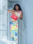Woman in a colorful dress holding a red Elyse & i Finn Scallop clutch on a white railing.