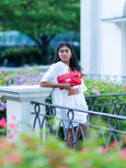 Woman in a white outfit holding a red Elyse & i Finn Scallop clutch in a garden setting