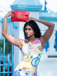Woman holding a red Elyse & i Finn Scallop clutch in front of a blue architectural background