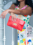 Person holding a red Elyse & i Finn Scallop clutch bag with a colorful dress in the background