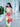 Woman holding a red Elyse & i Finn Scallop handbag in an outdoor setting with columns and plants.