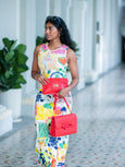 Woman holding a red Elyse & i Finn Scallop handbag in an outdoor setting with columns and plants.