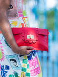 Person holding a red Elyse & i Finn Scallop clutch with a colorful dress in the background