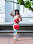 Woman holding a red Elyse & i Finn Scallop clutch in an outdoor setting