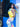 Woman in a colorful dress with a yellow Finn Elyse & i bag against a blue wall.