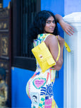 Woman in a colorful dress with a yellow Finn Elyse & i bag against a blue wall.