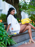 Woman in white outfit holding a yellow Finn Elyse & i clutch in a garden setting
