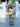Woman in a colorful dress holding a yellow Finn Elyse & i bag in front of a white gate.