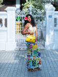 Woman in a colorful dress holding a yellow Finn Elyse & i bag in front of a white gate.