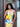 Woman wearing a colorful dress with a yellow Finn Elyse & i bag, standing in front of a wooden door.