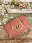 Pink Elyse & i Finn Scallop handbag with gold accents on a wooden surface with flowers in the background