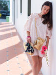 Girl in pink and white flouncy dress leaning on wall holding a gold bag and wearing a gold crossbody bag - the Luna by Elyse & i.