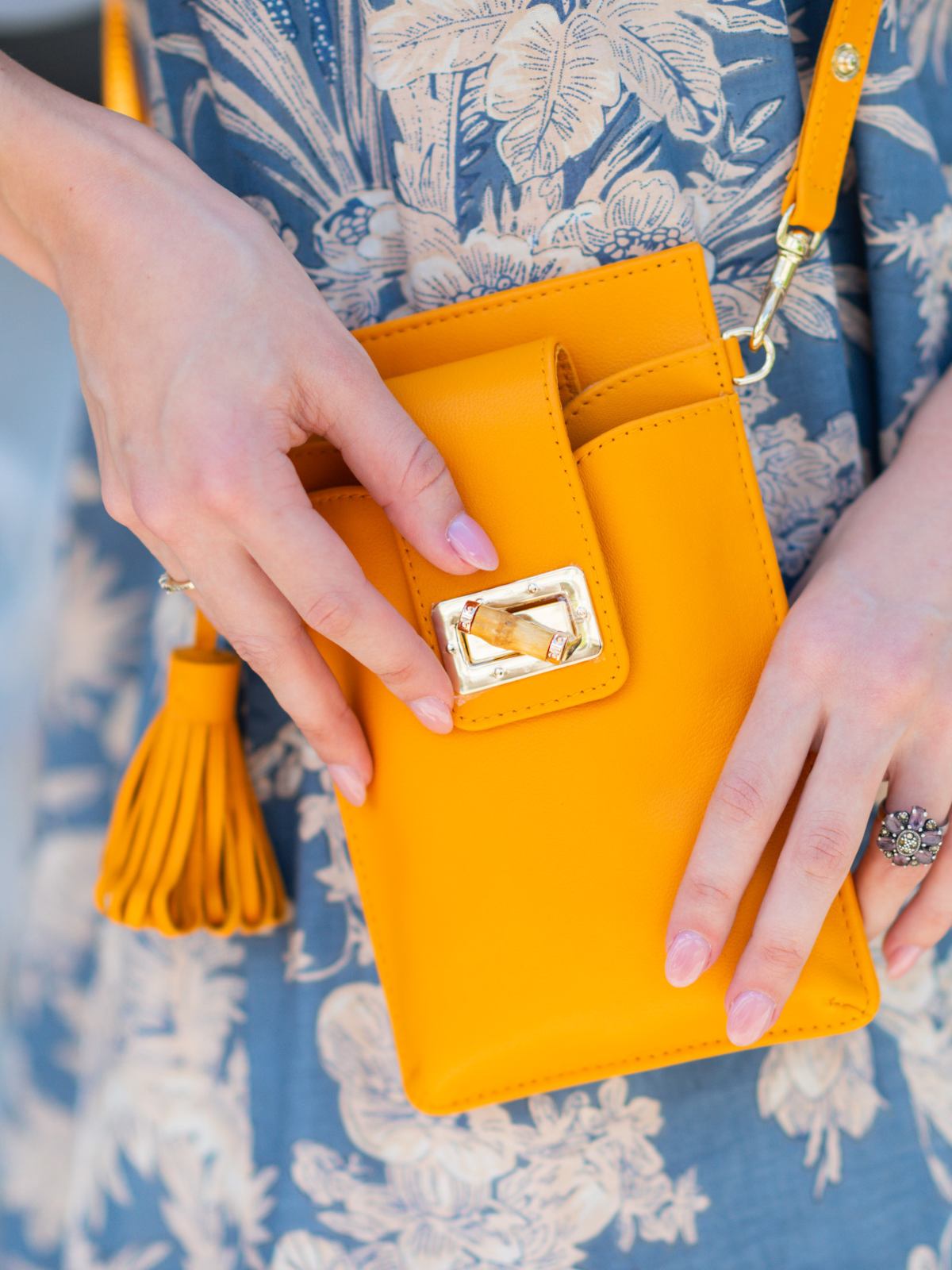 Elyse & i orange Luna Lock phone bag with decorative clasp held by hands on a floral-patterned fabric background