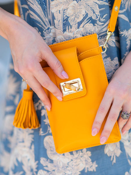 Elyse & i orange Luna Lock phone bag with decorative clasp held by hands on a floral-patterned fabric background