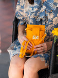 Person holding a bright orange Luna Lock by Elyse & i handbag with gold accents, wearing a blue floral dress.