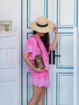 Woman in a pink dress with lace details holding a brown snakeprint phone bag by Elyse & i - with a straw hat standing in front of a white door with blue trim.