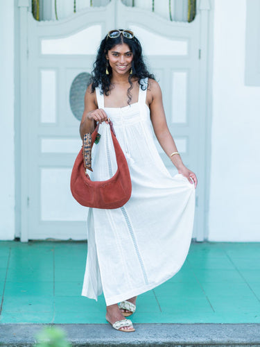 Woman in a white dress holding a brown Elyse & i Martha Suede Hobo bag in terracotta suede against a light blue wall.